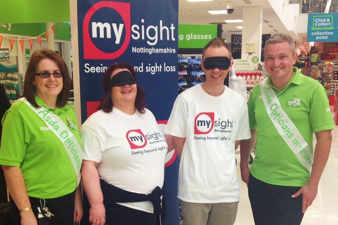 For volunteers stood in front of a My Sight Notts Banner in in the foyer of ASDA. Two are wearing blindfolds.