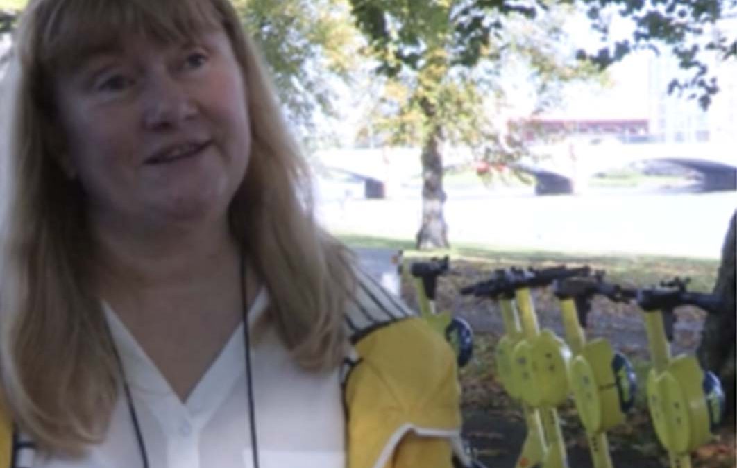 Woman in yellow jacket standing in from of a some e-Scooters