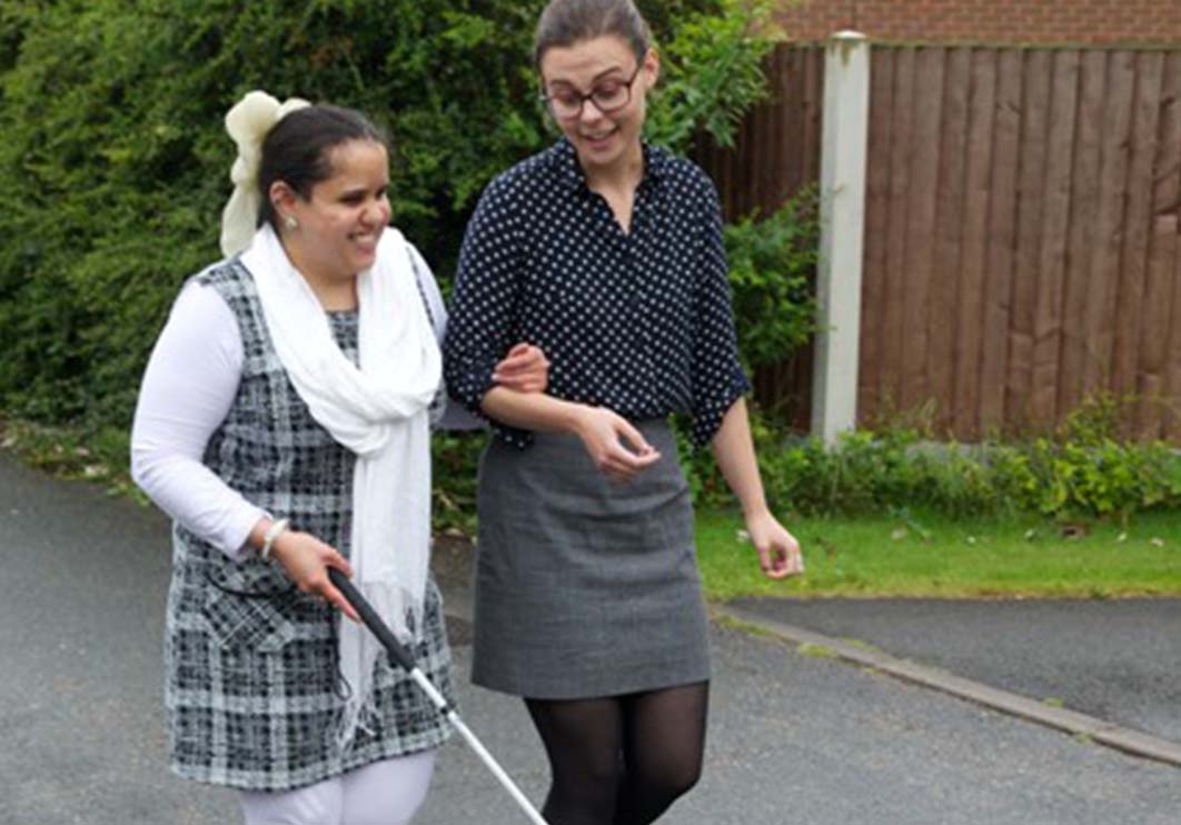 Female volunteer sighted guide assisting a woman with a white cane.