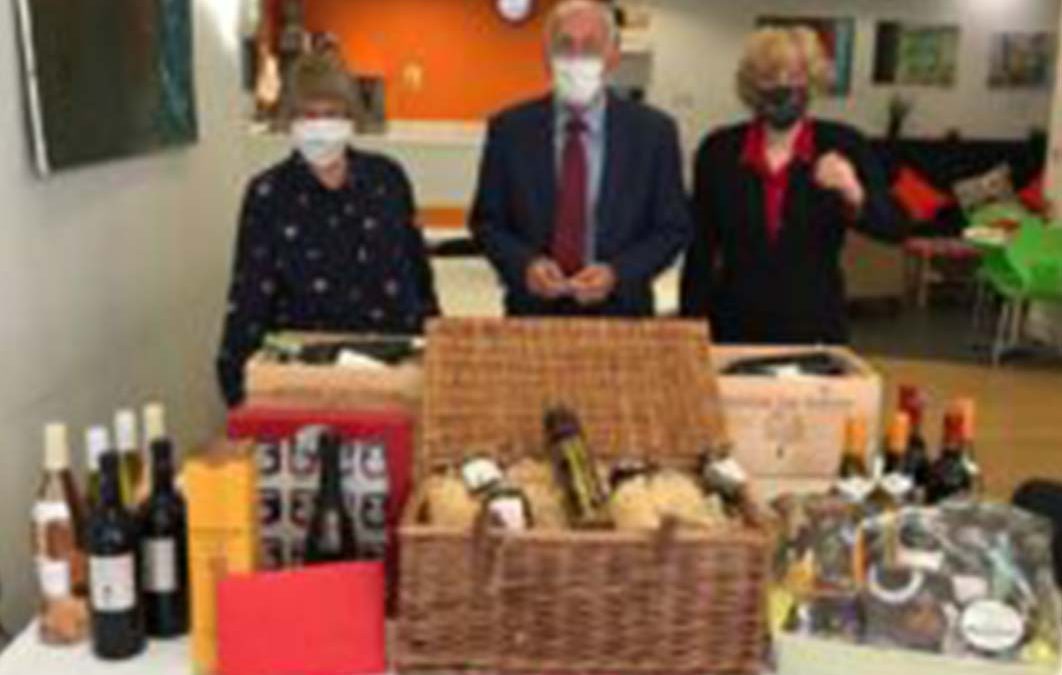 A man and two woman standing behind several hampers of food and drinks.