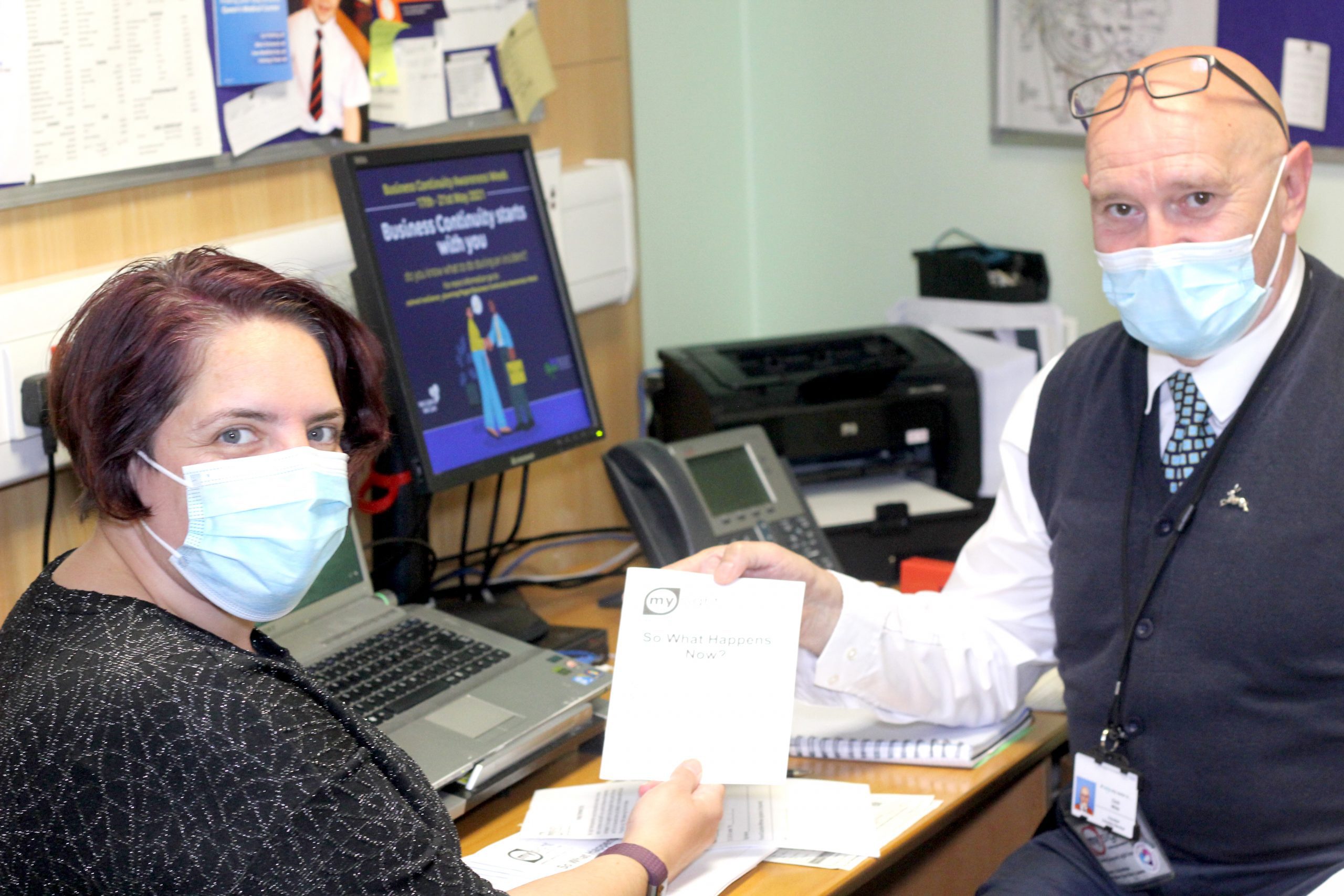 Eye Clinic Liaison Officer ECLO handing a woman a leaflet. Both are wearing face coverings.