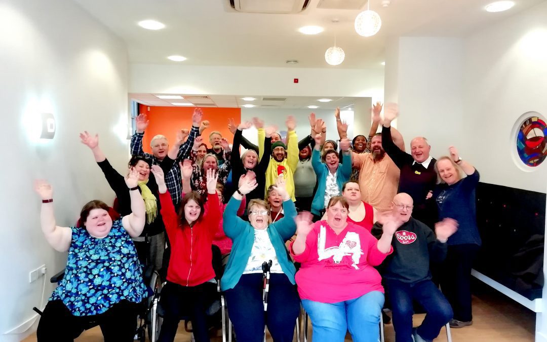 Group of over twenty people waving their hands in the air and cheering.