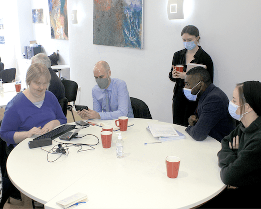 A woman using assistive technology. She is being interviewed by four people.