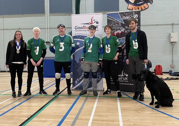 5 members of the Nottinghashire Sheriff’s Goalball Club novice team standing in a row with their silver medals around their necks. Also in the picture is Kirsty our coach and Arnold the black Labrador and honorary mascot! 5 members of the Nottinghashire Sheriff’s Goalball Club novice team standing in a row with their silver medals around their necks. Also in the picture is Kirsty our coach and Arnold the black Labrador and honorary mascot!