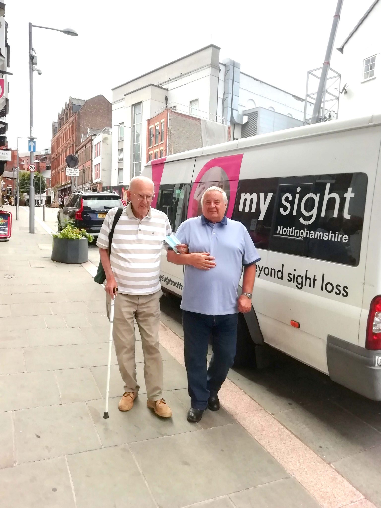 Image above shows a male volunteer sighted guide assisting a man with a white walking stick