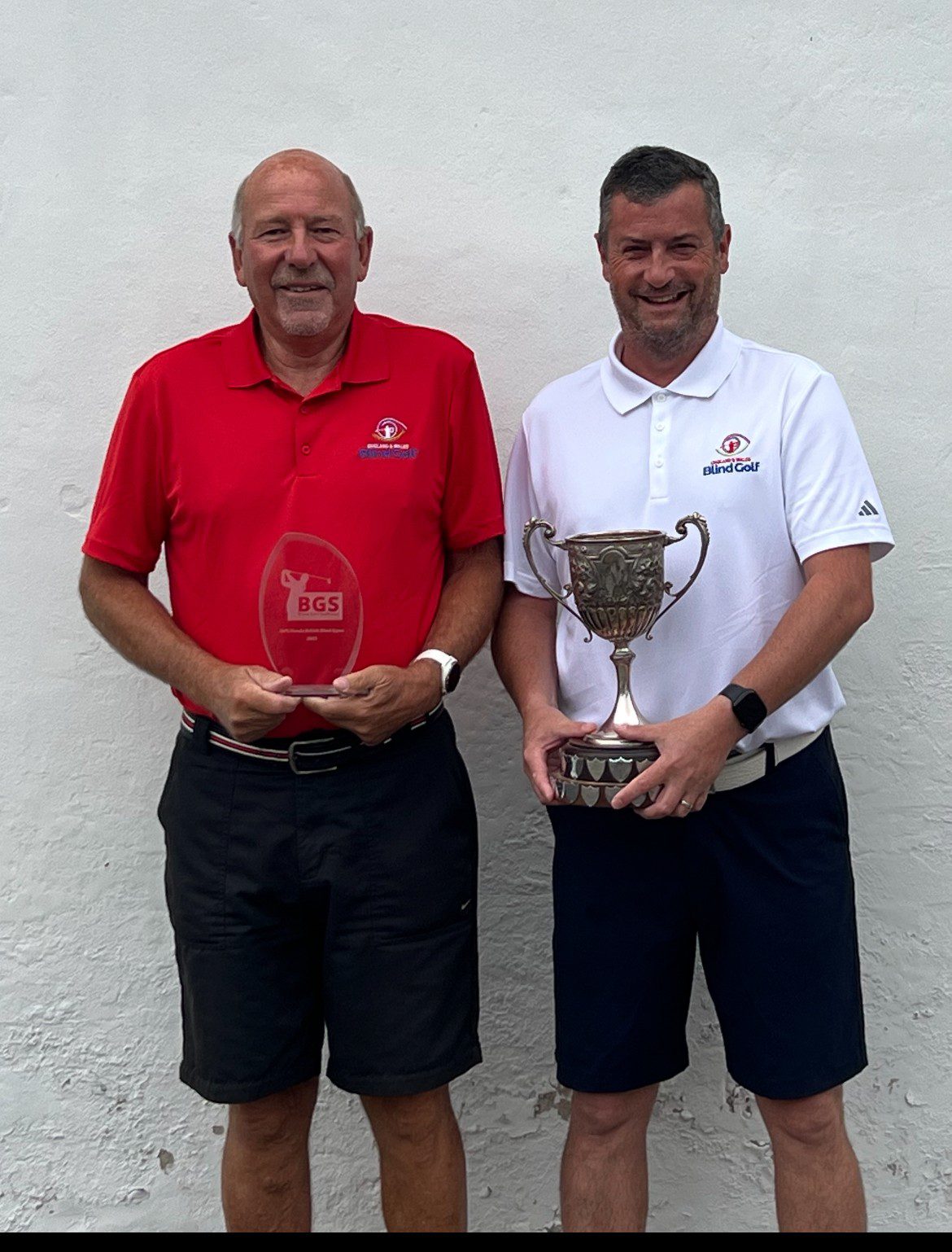 A woman laying on the floor of a Goal-ball court reaching for the ball. There is a man reaching for the ball behind her.